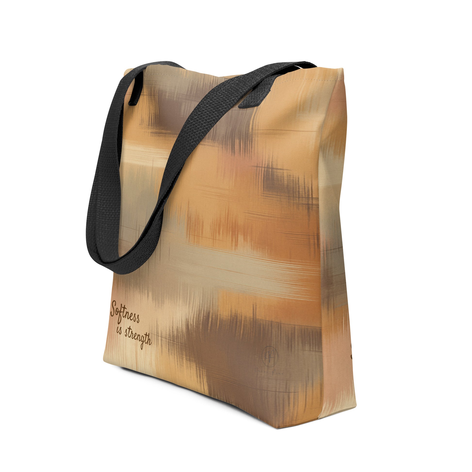 Beige and brown patterned tote bag with black handles and the phrase “Softness is strength” printed on the bottom right.