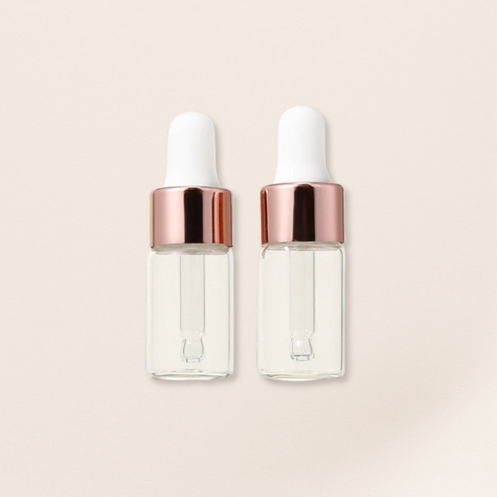 Two clear glass dropper bottles with rose gold caps on a beige background