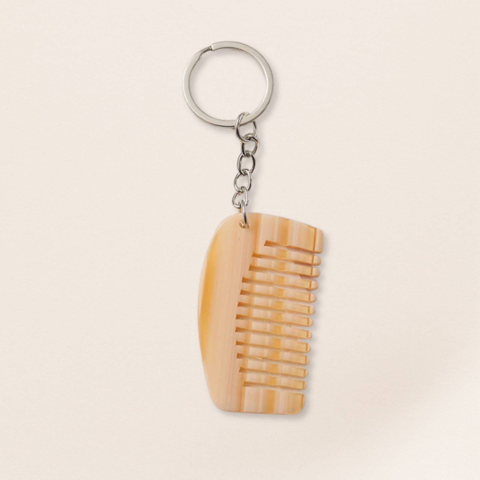 Mini cream marbled comb keyring with silver chain on a beige background.