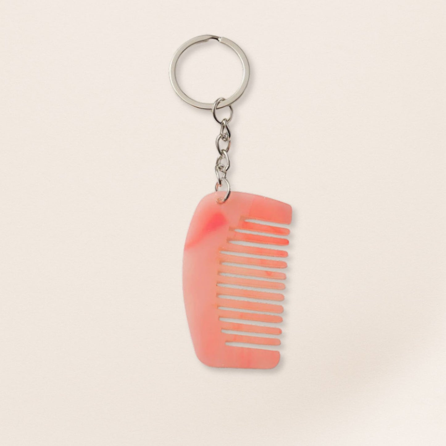 Mini pink marbled comb keyring with silver chain on a beige background.