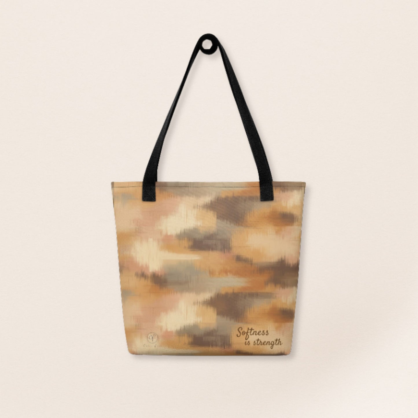 Beige and brown patterned tote bag with black handles and the phrase “Softness is strength” printed on the bottom right.
