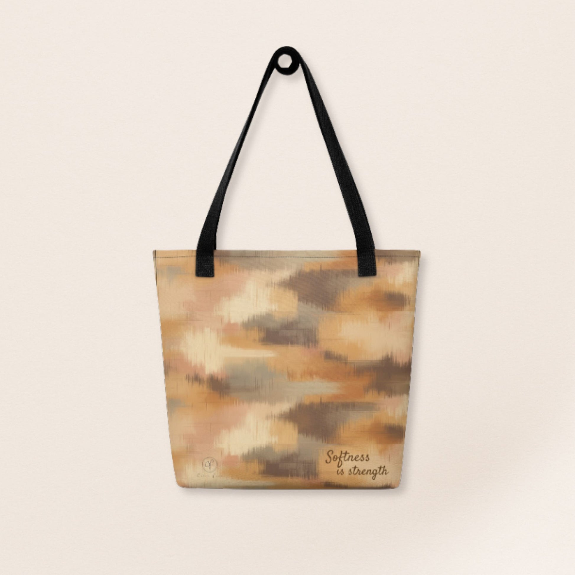 Beige and brown patterned tote bag with black handles and the phrase “Softness is strength” printed on the bottom right.