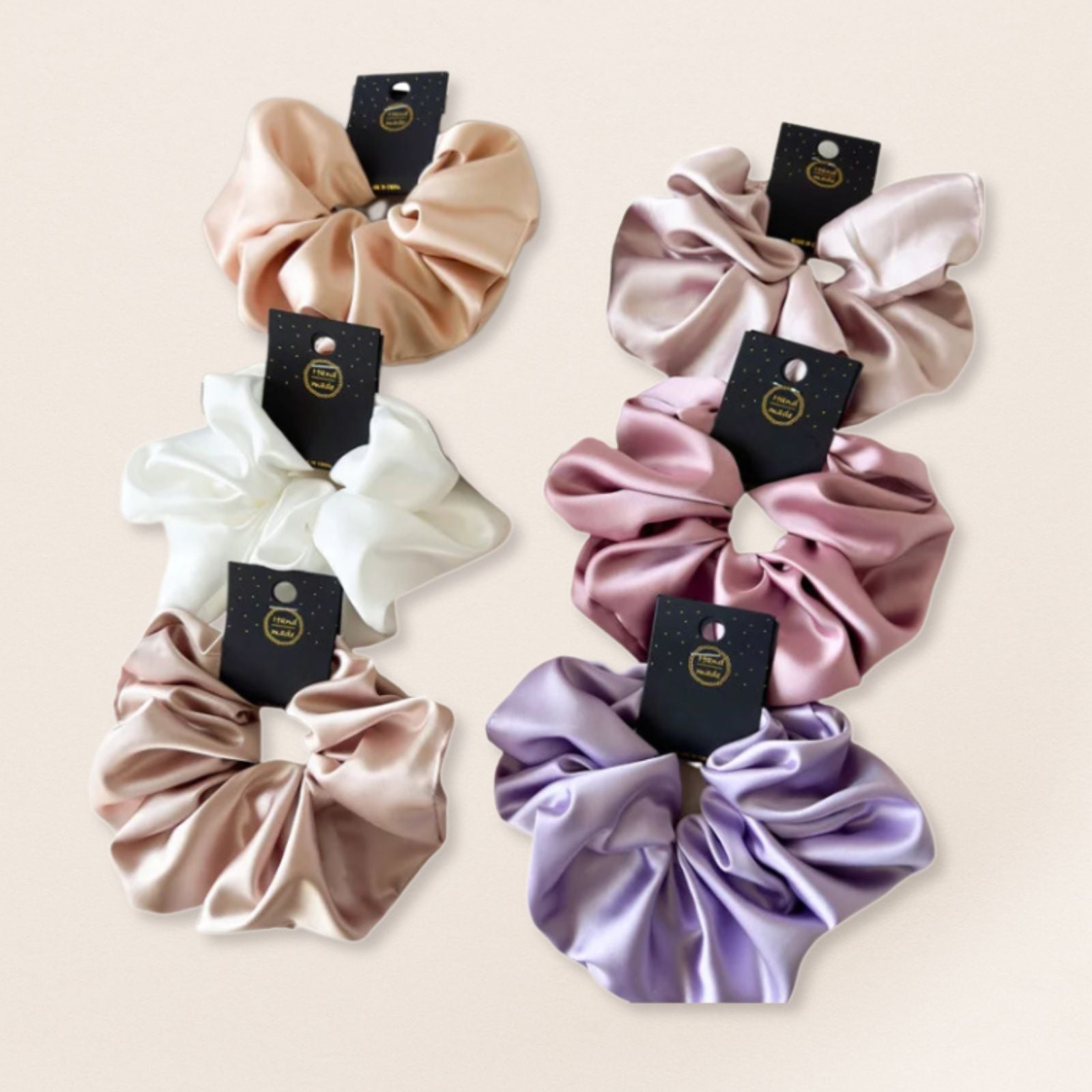 Set of four satin scrunchies in different colors with tags on a beige background