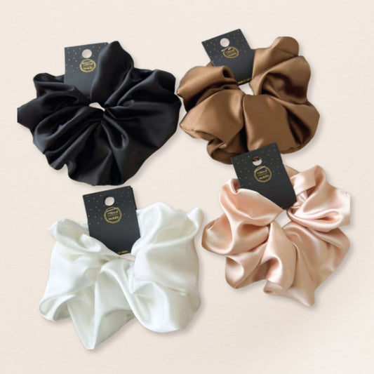 Four satin scrunchies in black, brown, white, and beige on a light beige background.