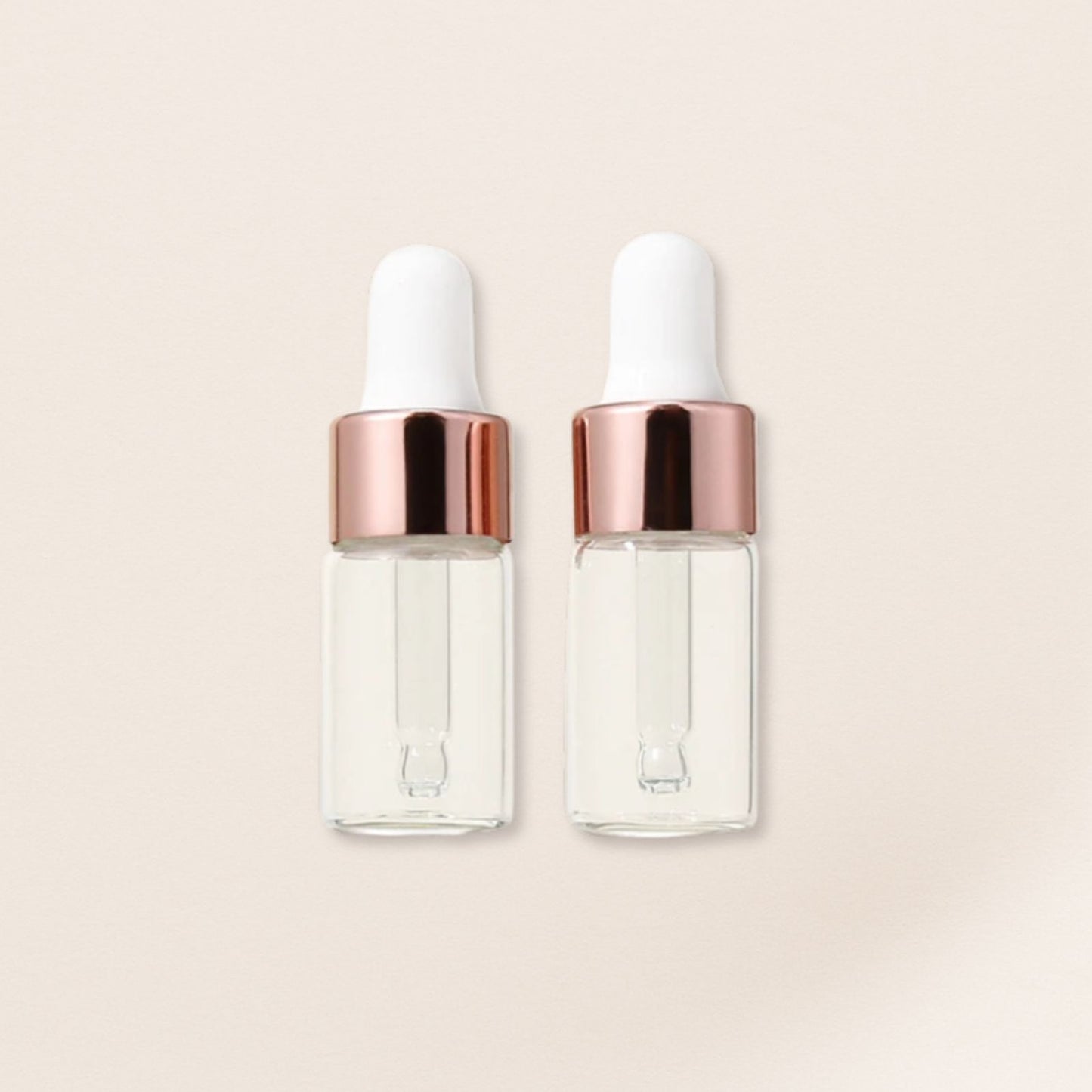 Two clear glass dropper bottles with rose gold caps on a beige background