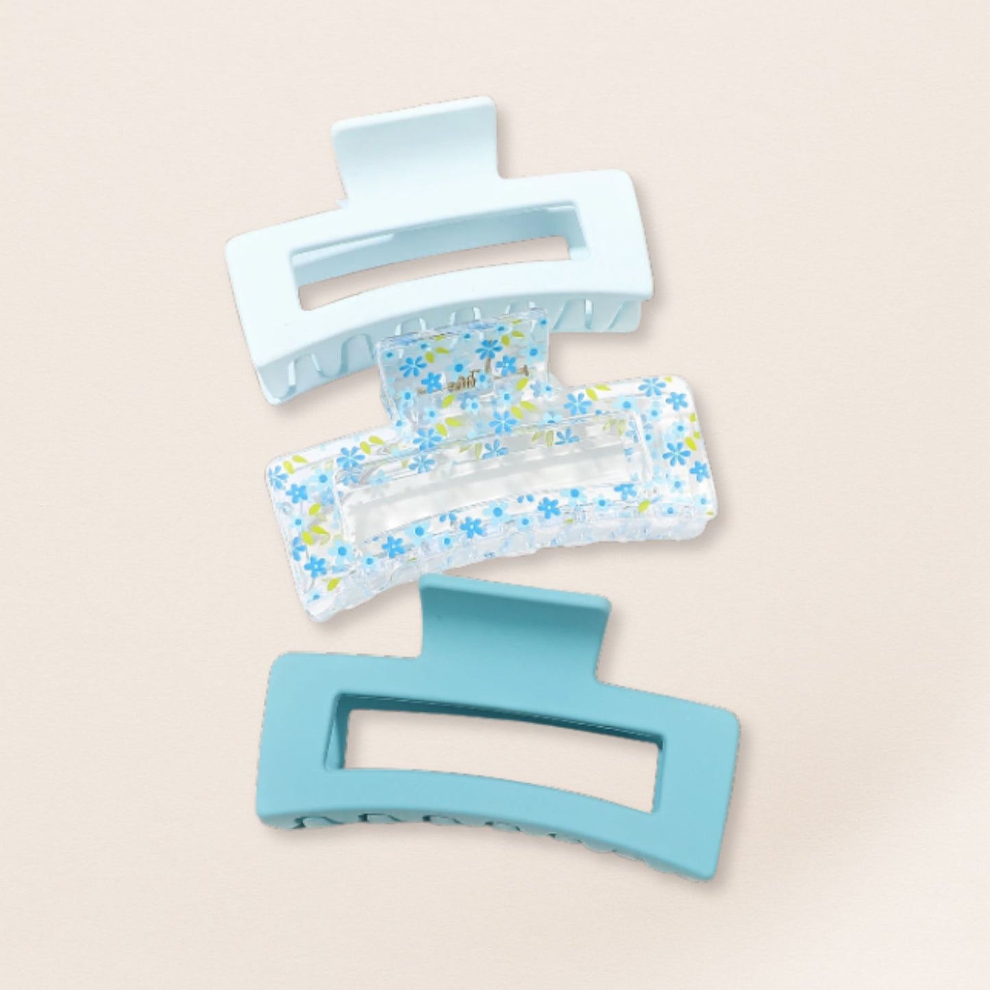 Two blue hair clips, one plain and one with floral pattern, on a beige background