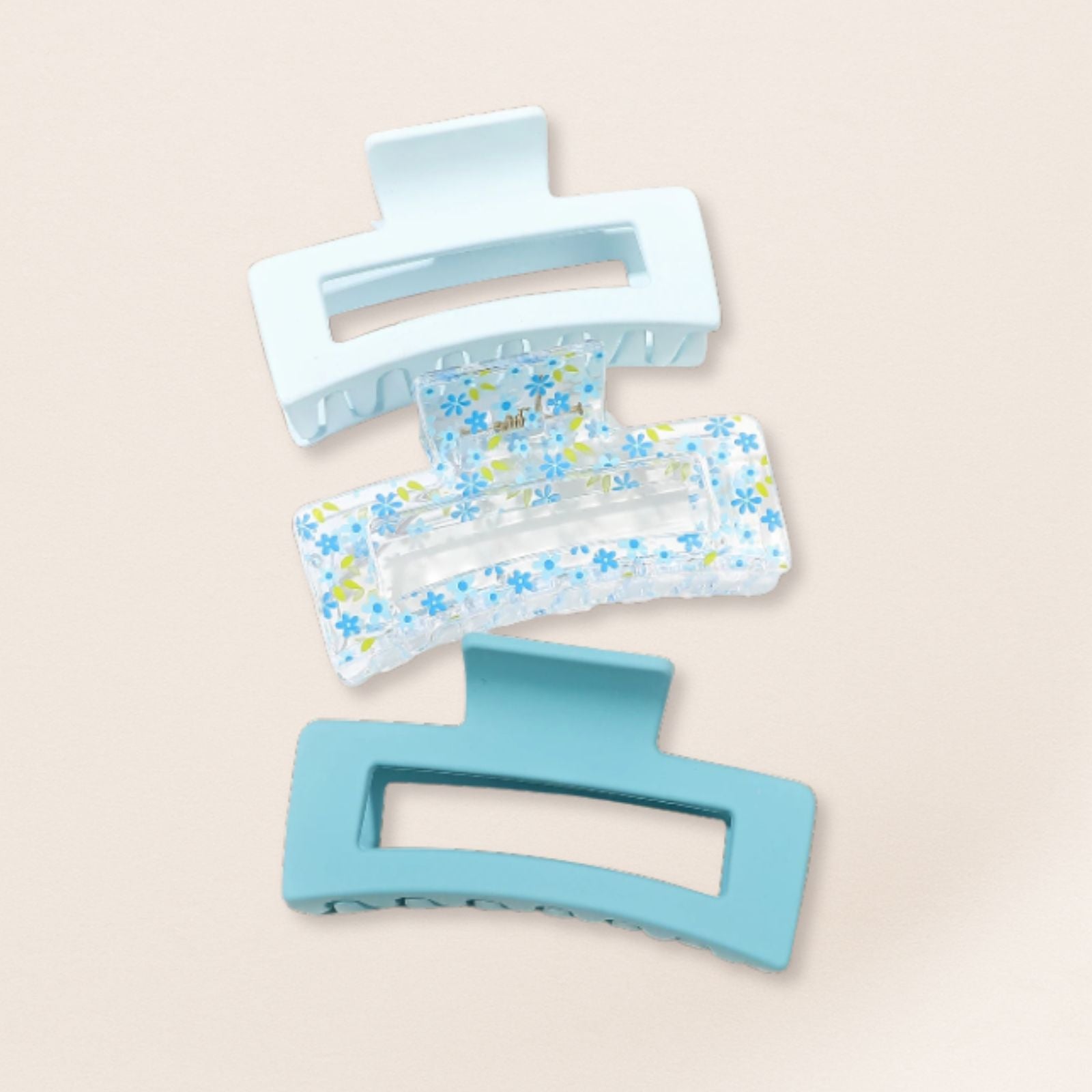 Two blue hair clips, one plain and one with floral pattern, on a beige background