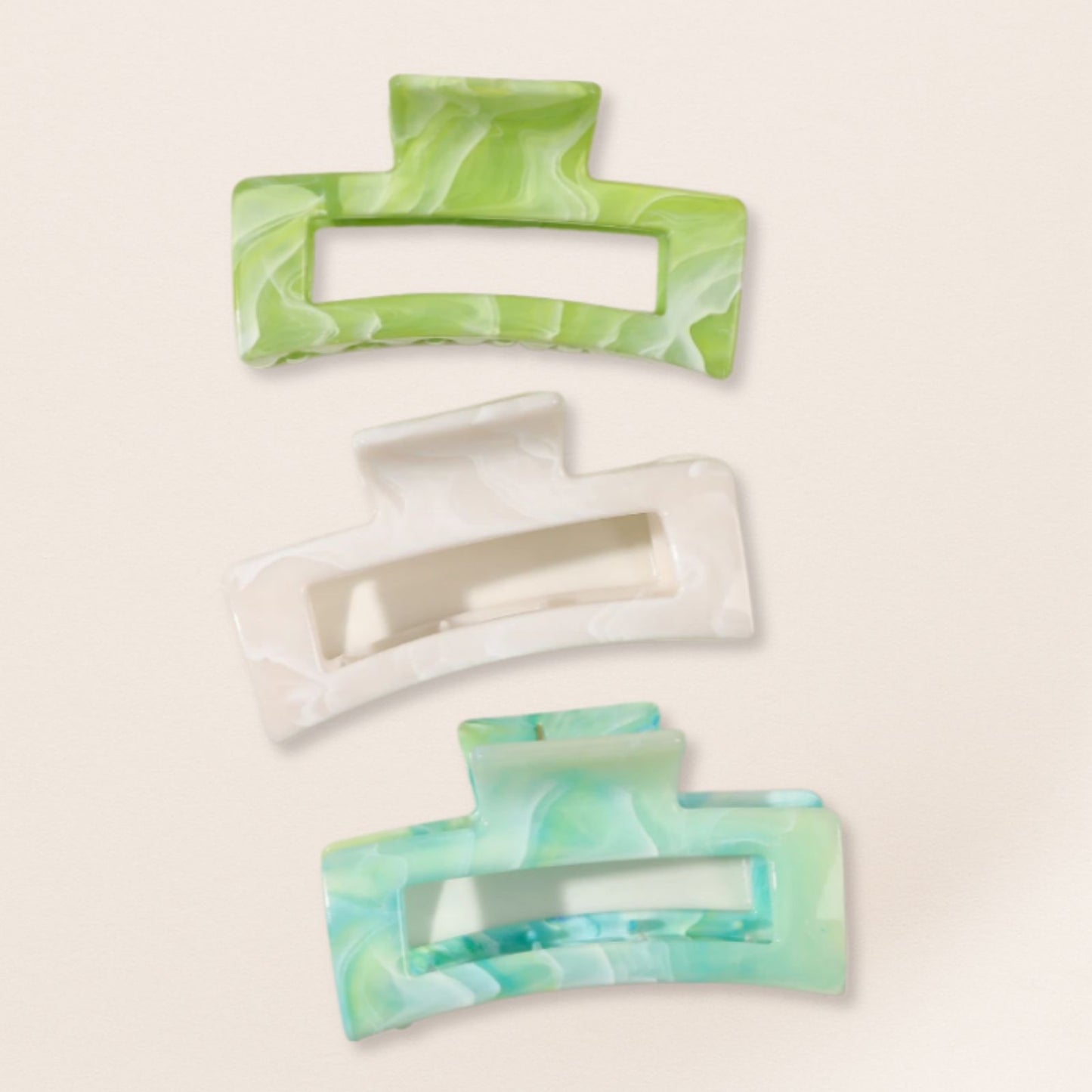 Three rectangular hair clips with green and white marbled design on a beige background