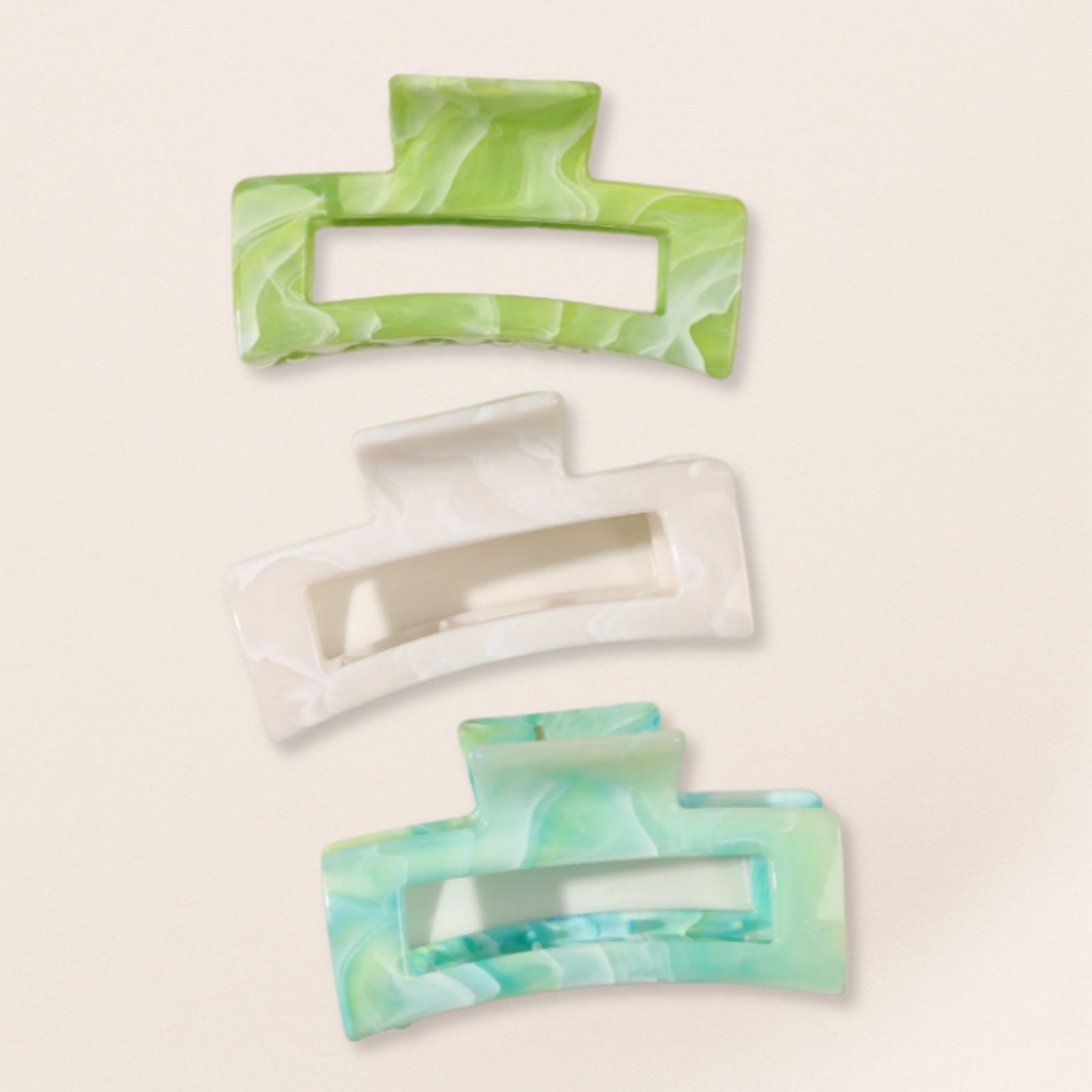 Three rectangular hair clips with green and white marbled design on a beige background