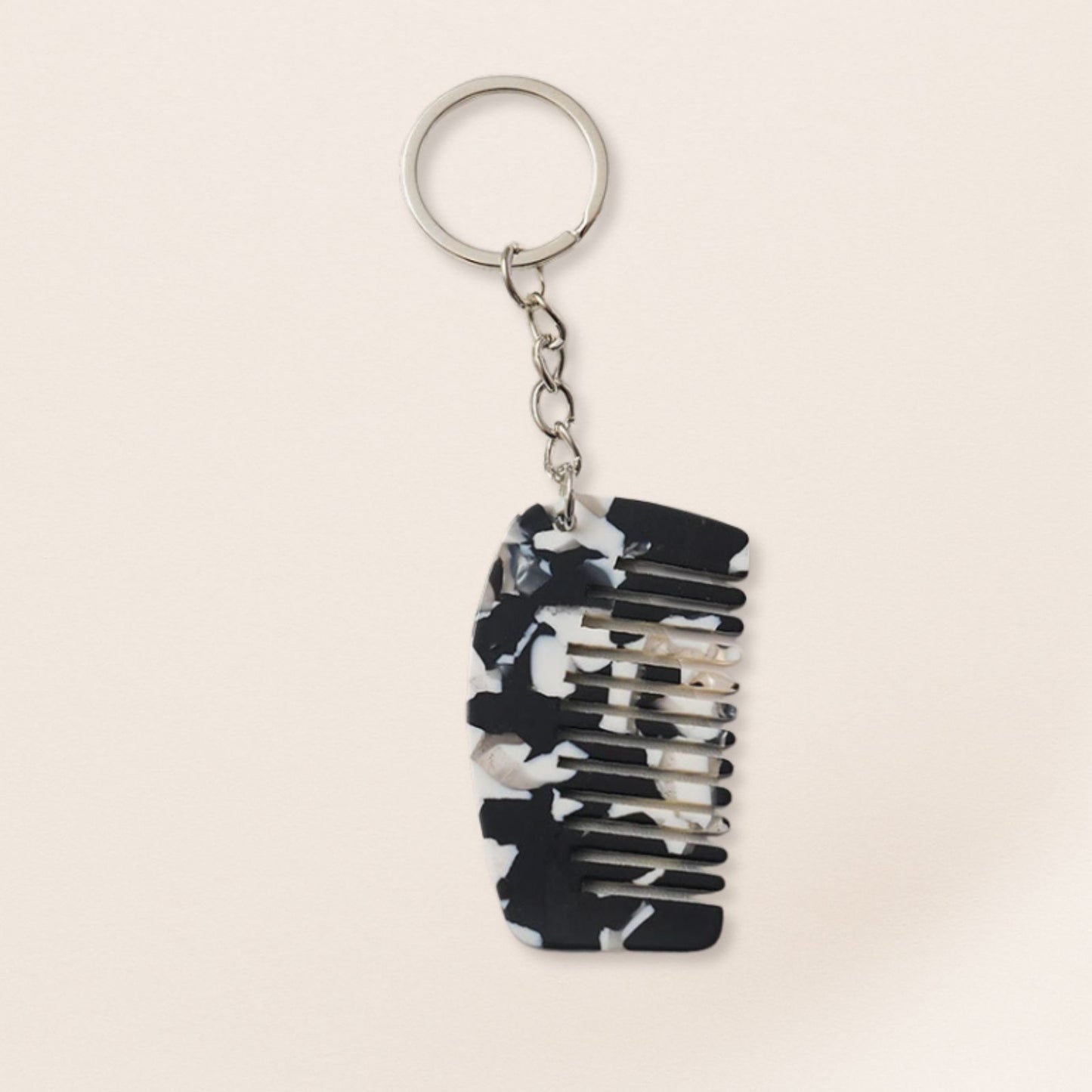 Mini black marbled comb keyring with silver chain on a beige background.