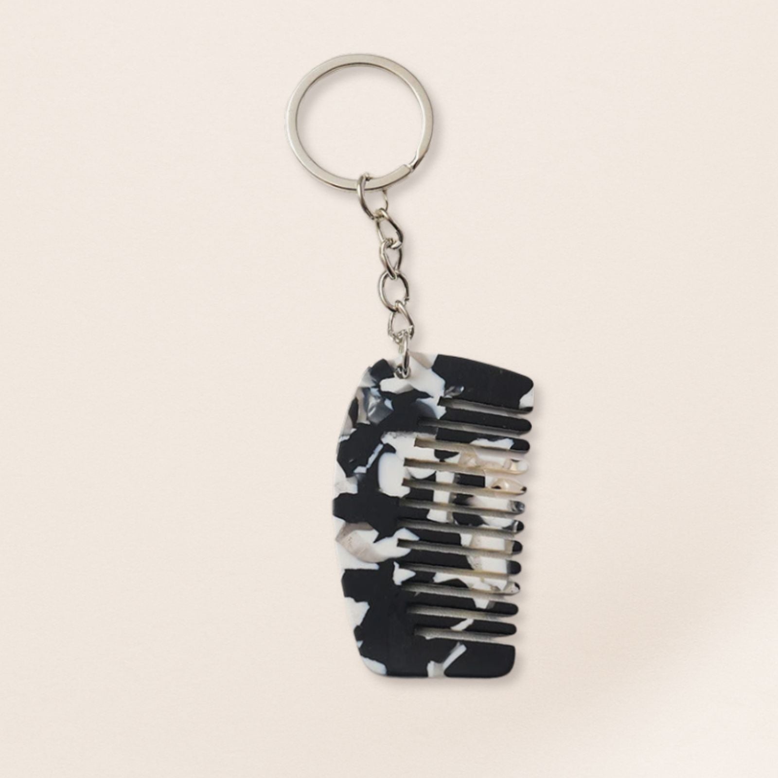 Mini black marbled comb keyring with silver chain on a beige background.