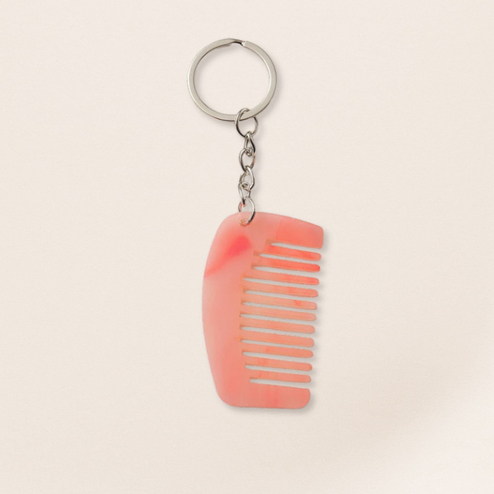 Mini pink marbled comb keyring with silver chain on a beige background.