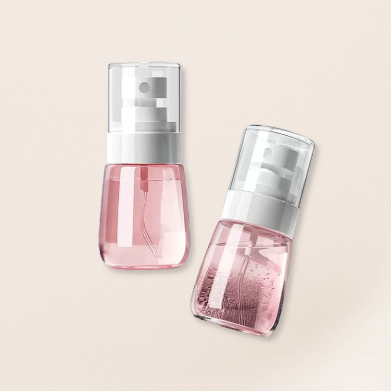 Two pink spray skincare bottles with silver caps on a beige background