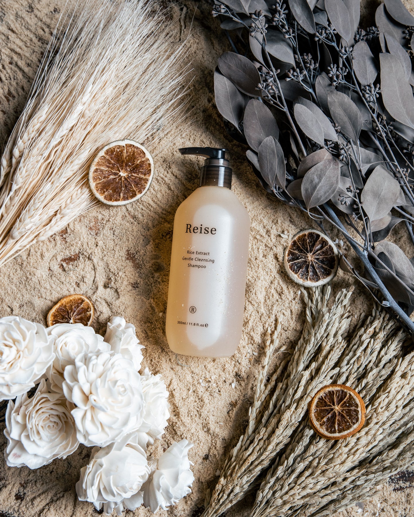 Reise shampoo bottle on a textured surface with flowers and dried elements